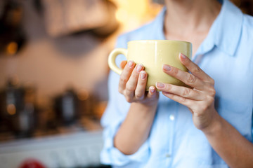 Graceful female hands hold cup of coffee. Young woman is drinking tea in cozy home kitchen. Close up.