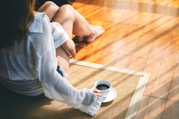 Top view image of a woman sitting and holding a cup of hot coffee on the floor in the morning