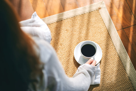Top view image of a woman sitting and holding a cup of hot coffee on the floor in the morning