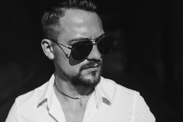 Portrait close up of handsome young businessman. Man dressed in white shirt and sunglasses on the grunge background. Black and white