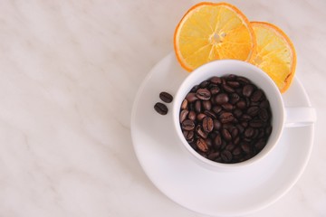 White Cup and saucer, coffee beans, slices of dried orange on a gray table, top view