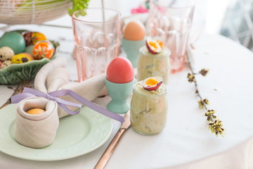 Easter egg wrapped in a linen napkin shaped like bunny ears on Easter breakfast table. Green pea pate in a glass jar with quail egg.