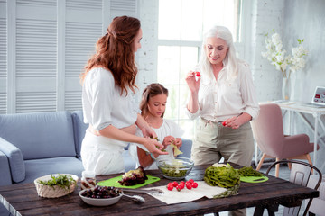 Grey-haired elderly woman helping her pregnant daughter cooking salad