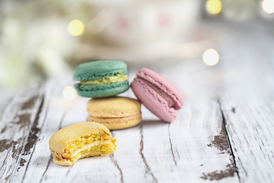 Bite missing from a lemon french macaron in front of a stack of macarons on a white rustic table.