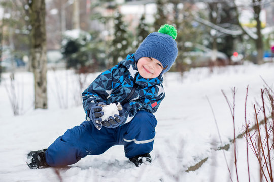 Happy little boy sculpts snowballs in the park.