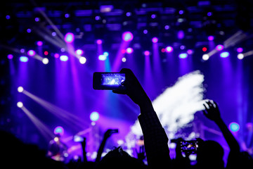 Smartphone in hand at a concert, blue light from stage