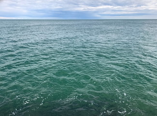 Panorama of a small ripple on the azure surface of the Black Sea, endlessly stretching to the horizon under the cloudy spring sky.