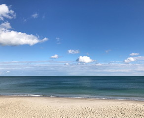 A panorama of a clean sandy shore near the dark blue of the Black Sea against the background of a shallow blue sky.