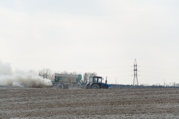 Fototapeta na wymiar Tractor fertilizes agricultural field in spring