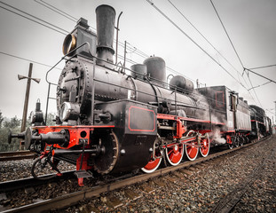 Fototapeta na wymiar Old steam engine locomotive with puffs of white steam passes a turn on the railroad