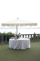 wedding garden party set: white table and sun umbrella in an elegant garden ready for the party