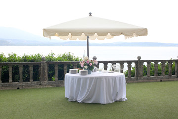 wedding garden party set: white table and sun umbrella in an elegant garden ready for the party