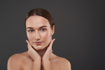 Charming young woman with natural makeup keeping hands on her neck