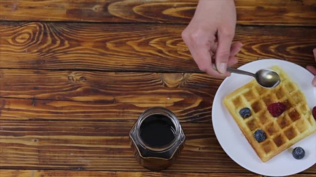 Woman pouring maple syrup on tasty waffles