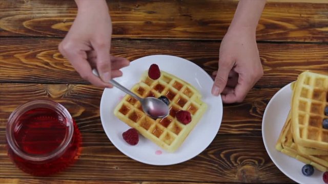 Woman pouring straberry sauce onto tasty homemade waffles, closeup