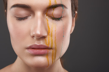 Serene young lady with orange and blue liquid dripping from her face