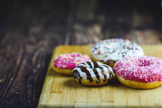 Sweet and tasty donuts with different sprinkles. Assorted donuts with chocolate frosted, pink glazed and sprinkles donuts. Donuts on a wooden background and space for text. Horizontal. Toned picture.