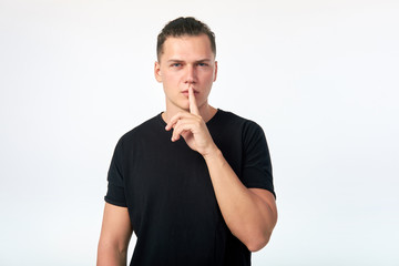 Young attractive man holding index finger near the lips on a white background. Man asking to keep silence.