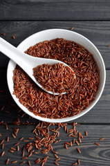 red rice in a ceramic bowl with spoon against dark wooden background