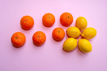 Fresh organic tangerines and yellow lemons on pink background, top view