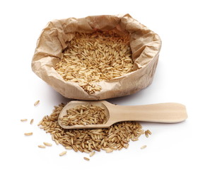 Peeled oat grains in paper bag with wooden spoon isolated on white background