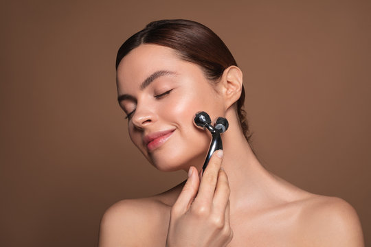 Pleased woman massaging her face with face massager