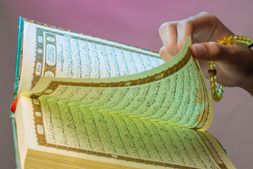 Al-Qur'an. Open Qur'an sheet by the hand holding the prayer beads (tasbih).