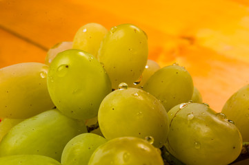 large brush of green grapes in a red ceramic plate on a wooden background
