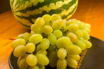 large brush of green grapes and watermelon in a dark ceramic plate on a wooden background