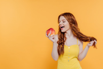 beautiful redhead girl biting apple isolated on yellow with copy space
