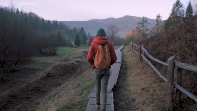 prety woman tourist walking on the wooden trail between rocks in the national park at sunrise with rocks background, back view. Excursion in Tustan, Ukraine. Tustan is a unique monument of history and
