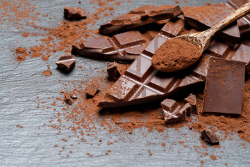Dark or milk organic chocolate pieces and cocoa powder on dark concrete backgound