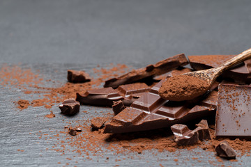 Dark or milk organic chocolate pieces and cocoa powder on dark concrete backgound