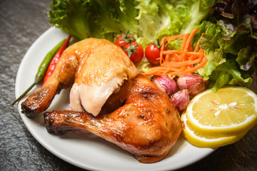 Roasted chicken legs on white plate with lemon chilli spicy herbs spices and salad lettuce vegetable