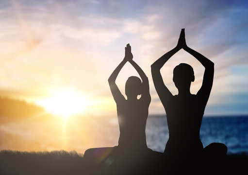 Mindfulness, Spirituality And Outdoor Yoga - Silhouettes Of Couple Meditating In Lotus Pose Over Sunset And Sea Background