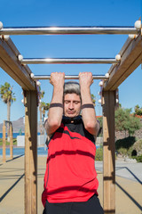Man practicing sports, calisthenics, in the urban gym outdoors, near the coast, with blue sky and palm trees around.