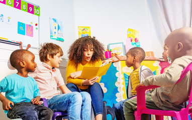 Teacher reads a book to group of kids in nursery