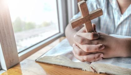 Close up hands of boy holding christian cross and praying on holy bible. religion concept.