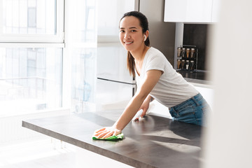 Portrait of pretty asian girl cleaning table with detergent and rag in kitchen at home