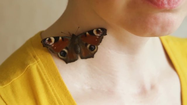 A live butterfly on the shoulder of a white woman.  The insect symbolizes the soul or organ (thyroid). Real time, close-up.