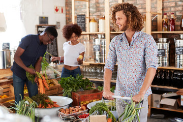Shoppers Buying Fresh Fruit And Vegetables In Sustainable Plastic Free Grocery Store