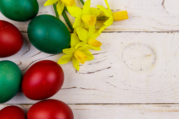 Painted Easter eggs and yellow daffodils on white wooden background. Easter composition. Top view, copy space