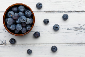 blueberries spilling out of a bowl on distressed white wood