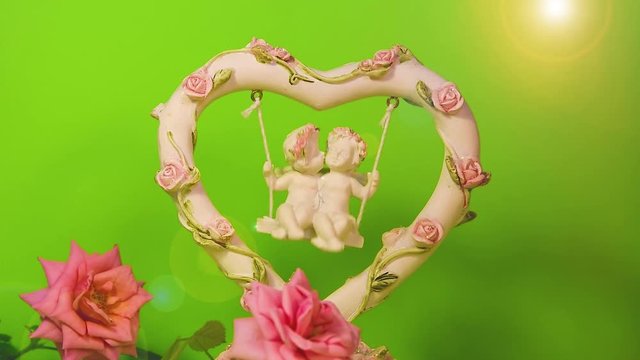 Two angels kissing and swinging on a swing with slow motion, clay figurine with natural rose flowers, festive romantic Valentine's day background