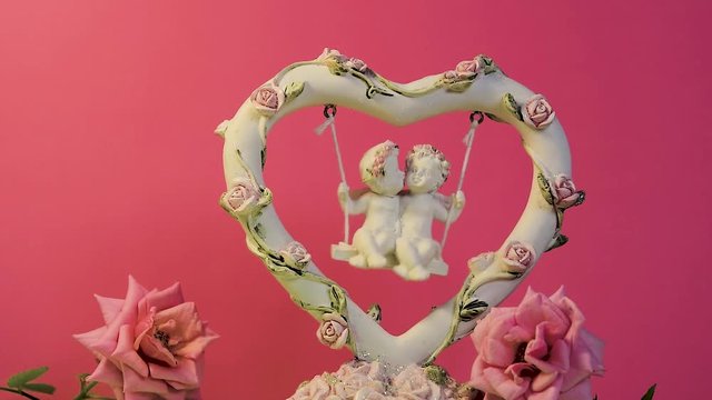 Two angels kissing and swinging on a swing with slow motion, clay figurine with natural rose flowers, festive romantic Valentine's day background
