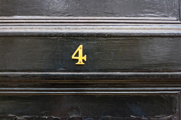 House number 4 with the four in bronze on a black door with horizontal lines