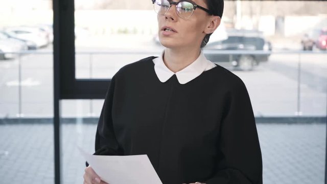 attractive worried woman in glasses pointing with finger while reading resume and learning then smiling before job interview  