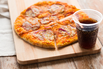 fast food and unhealthy eating concept - close up of sliced homemade pizza with cup of cola drink on wooden table