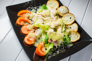 Caesar salad with bacon and quail eggs Black plate on a white wooden