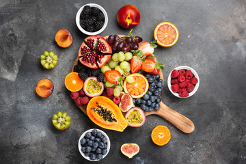Delicious fruit platter pomegranate papaya oranges passion fruits berries on wooden board on dark concrete background, selective focus